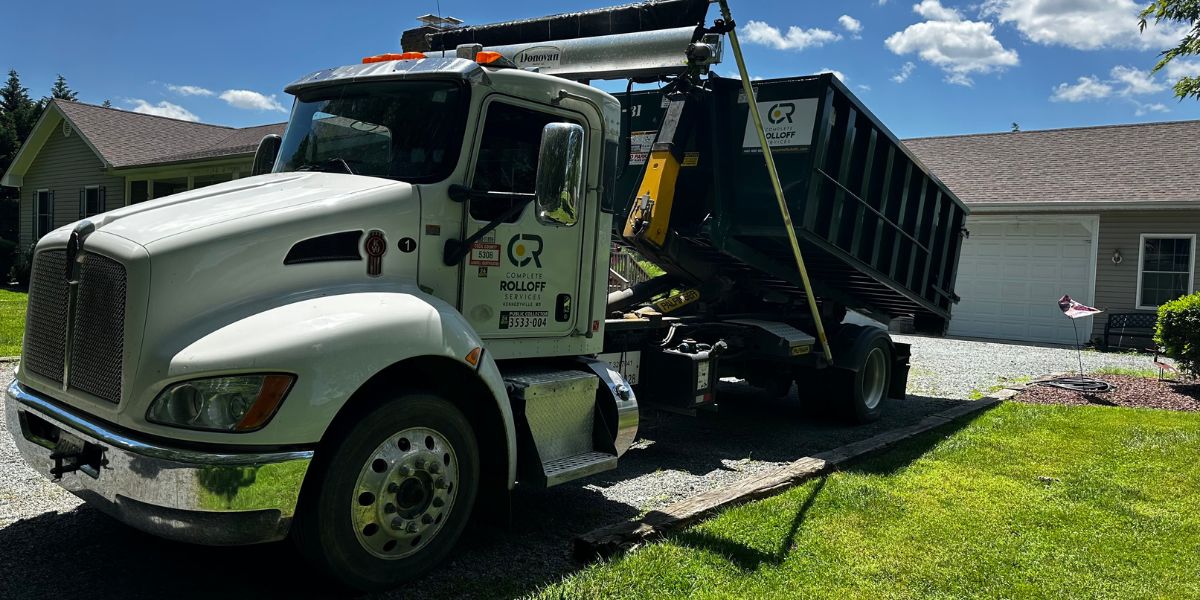 A complete rolloff services truck delivering a 10 yard dumpster rental in a driveway of a home